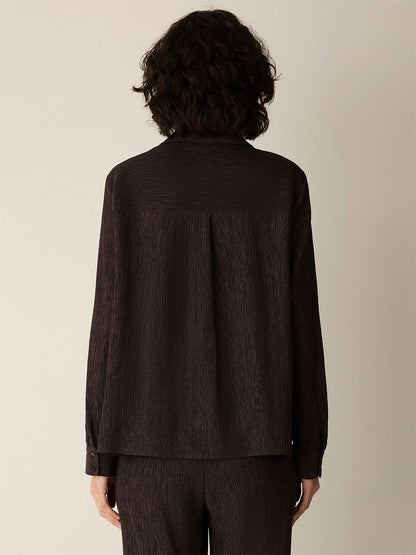 Person with short, curly dark hair wearing the Eileen Fisher Woven Plissé Classic Collar Shirt in Truffle, facing away from the camera against a plain light background.
