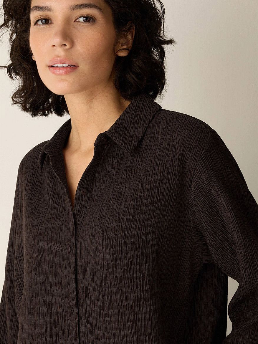 A woman with short, wavy dark hair wears the Eileen Fisher Woven Plissé Classic Collar Shirt in Truffle and looks toward the camera against a neutral background.