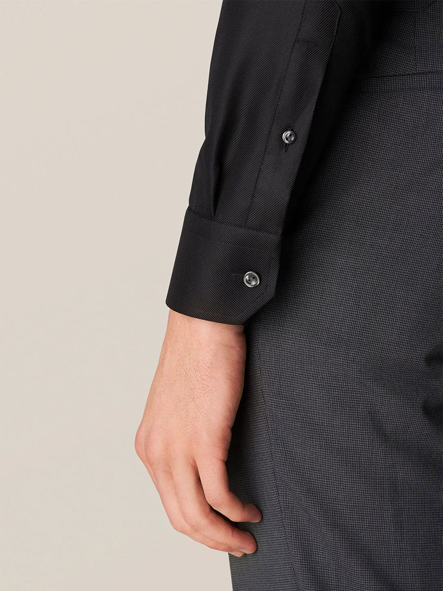 Wearing an Eton Slim Fit Black Textured Twill Dress Shirt and dark pants, a person stands with their hand relaxed by their side.