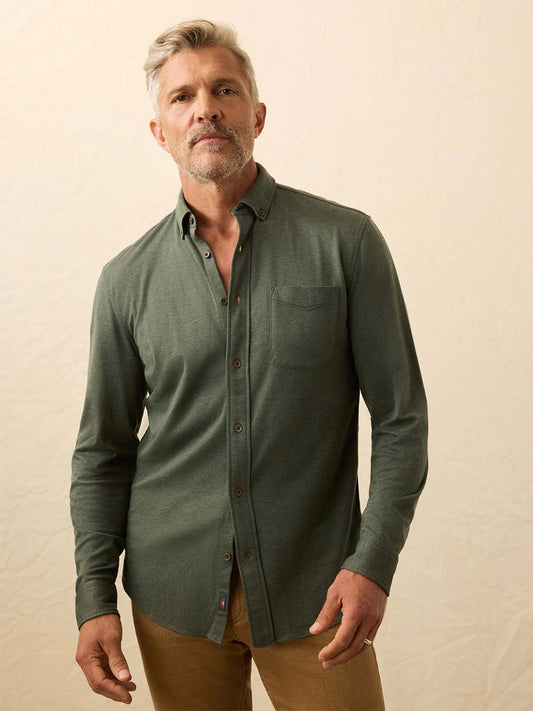 Man with short gray hair and beard wearing the Faherty Brand Coastline Knit Shirt in Forest Heather Twill and brown pants, standing against a neutral background.
