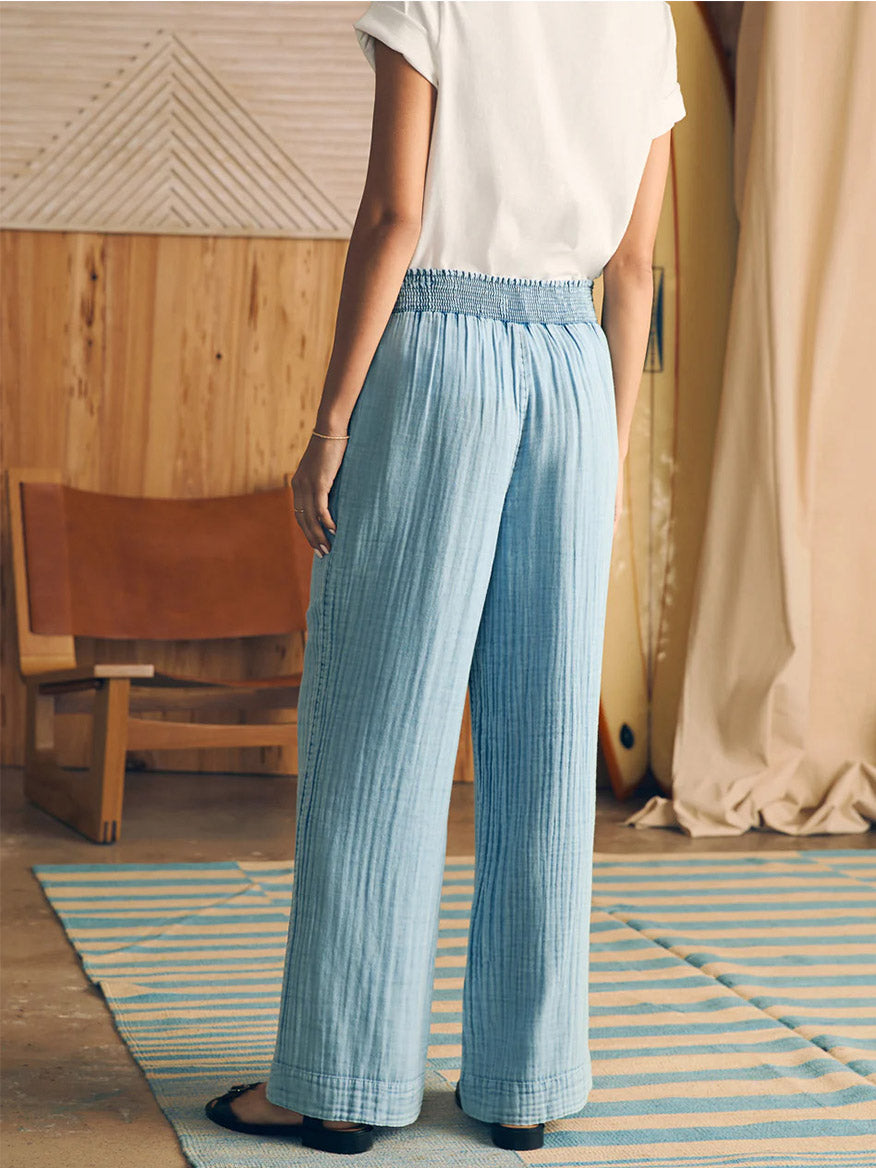 Woman standing in a room wearing Faherty Brand Dream Cotton Gauze Wide Leg Pant in Light Indigo Wash and a white t-shirt made of organic double gauze fabric.