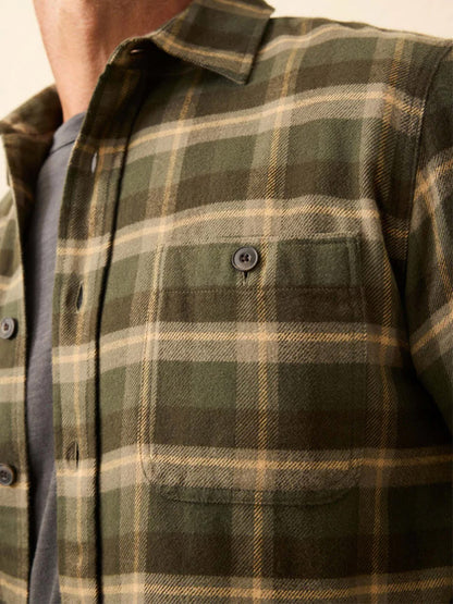 Close-up of a person wearing the Faherty Brand Heirloom Portuguese Flannel Shirt in Garrett Verde Plaid over a gray t-shirt, highlighting its chest pocket and button details.