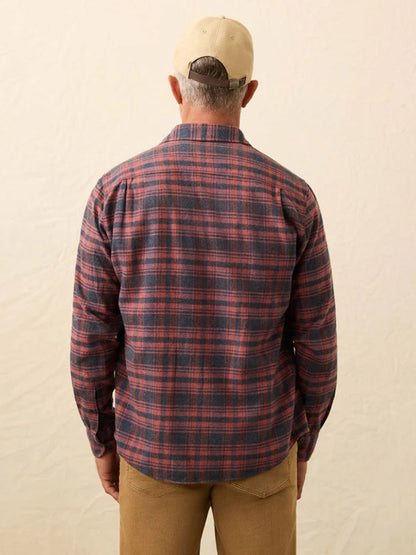 A man faces away against a plain light background, wearing a beige cap, classic fit tan pants, and the Faherty Brand Heirloom Portuguese Flannel Shirt in Porto Covo Plaid (red and blue).