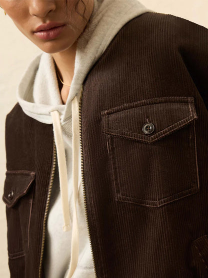 A person wearing a white hoodie under the Faherty Brand Heritage Cord Jacket in Chocolate Brown, featuring front flap pockets and a zipper—perfect for casual fall style.