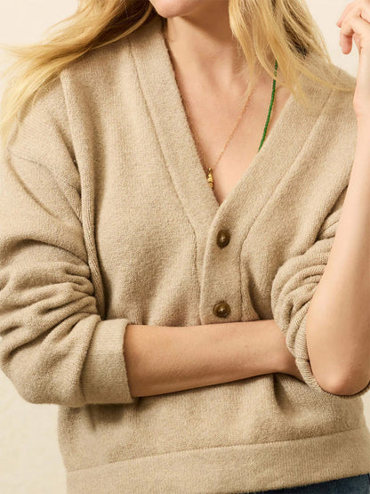 A person wears the Faherty Brand Jackson V-Neck Popover in Oatmeal Heather with rolled-up sleeves, a gold necklace, and a green string around the neck; their face is partially out of frame.