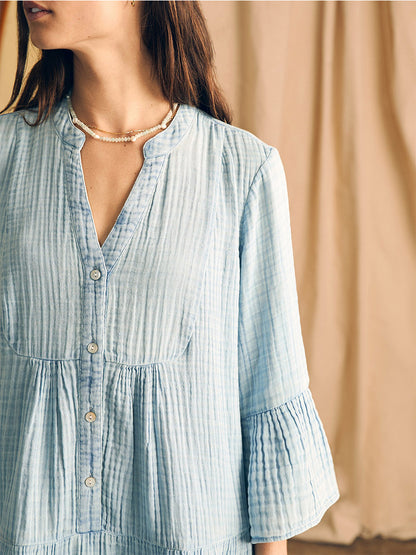 Woman wearing a Faherty Brand Dream Cotton Gauze Kasey Dress in Light Indigo Wash with long billowy sleeves, pleated details, and a necklace.