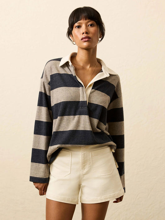 Woman standing against a plain background, wearing the Faherty Brand Legend™ Sweater Rugby Popover in Navy Rugby, featuring classic navy and beige stripes with a white collar, paired with cream-colored shorts.