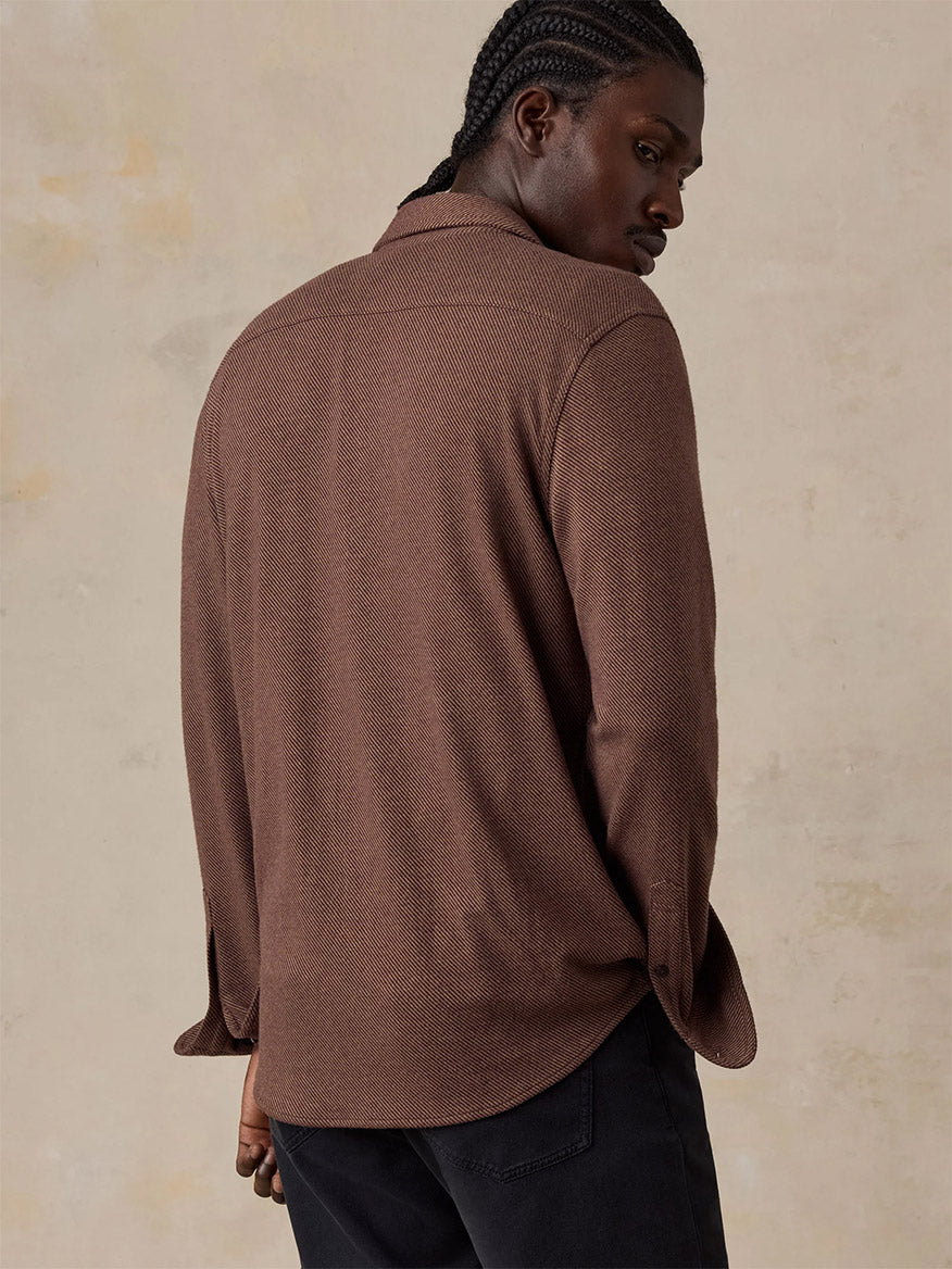 A man with braided hair wears the Faherty Brand Legend Sweater Shirt in Redwood Coast Twill and black pants, standing with his back to the camera against a neutral background.