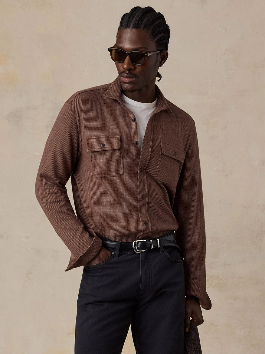 A man in sunglasses wears the Faherty Brand Legend Sweater Shirt in Redwood Coast Twill over a white tee with black pants, holding a coat against a neutral background.