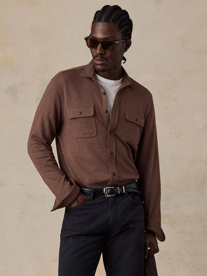 A man in sunglasses wears the Faherty Brand Legend Sweater Shirt in Redwood Coast Twill over a white tee with black pants, holding a coat against a neutral background.