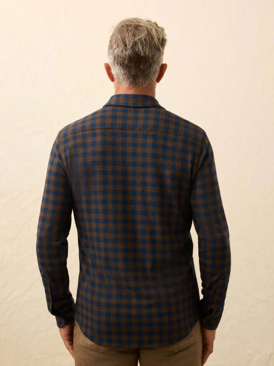 A man with gray hair, seen from behind, wears a Faherty Brand Legend Sweater Shirt in Woodland Check and beige pants against a light background.