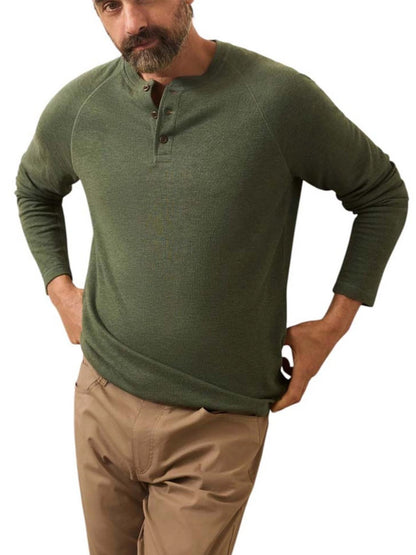 A man wearing a Faherty Brand Cloud Cotton Long-Sleeve Henley in Deep Fern Heather and tan pants stands with his hands on his hips against a white background.