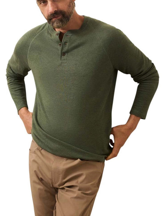 A man wearing a Faherty Brand Cloud Cotton Long-Sleeve Henley in Deep Fern Heather and tan pants stands with his hands on his hips against a white background.
