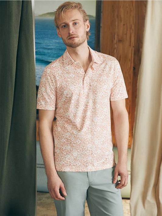 Man wearing a Faherty Brand Movement Short-Sleeve Polo in Hilo Rose Floral Print with vented hems and grey trousers standing indoors.