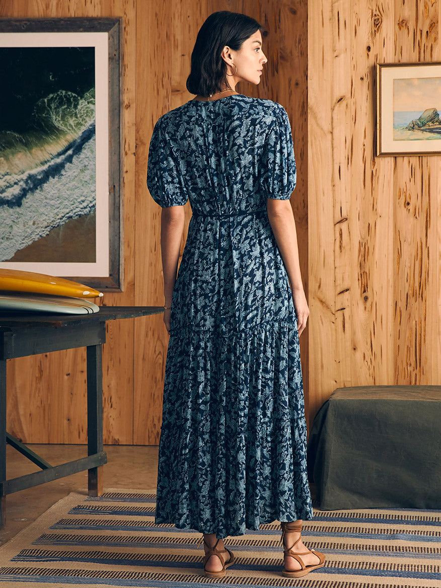 Woman in a Faherty Brand Orinda Maxi Dress in Blue Esna Floral standing in a room with wooden walls and artwork.