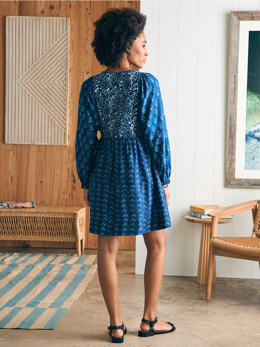 Woman in a Faherty Brand Silk Blend Solstice Mini Dress in Sunburst Mix Print standing in a stylish room, looking over her shoulder.