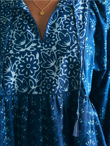 Close-up of a woman wearing a Faherty Brand Silk Blend Solstice Mini Dress in Sunburst Mix Print with a v-neckline, accessorized with a gold necklace.