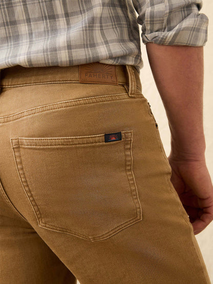 Close-up of a person wearing Faherty Brand Stretch Terry 5-Pocket Pant in Elk Brown with a gray plaid shirt, highlighting the back pocket's small logo tag, leather brand patch, and the pants’ authentic denim look.