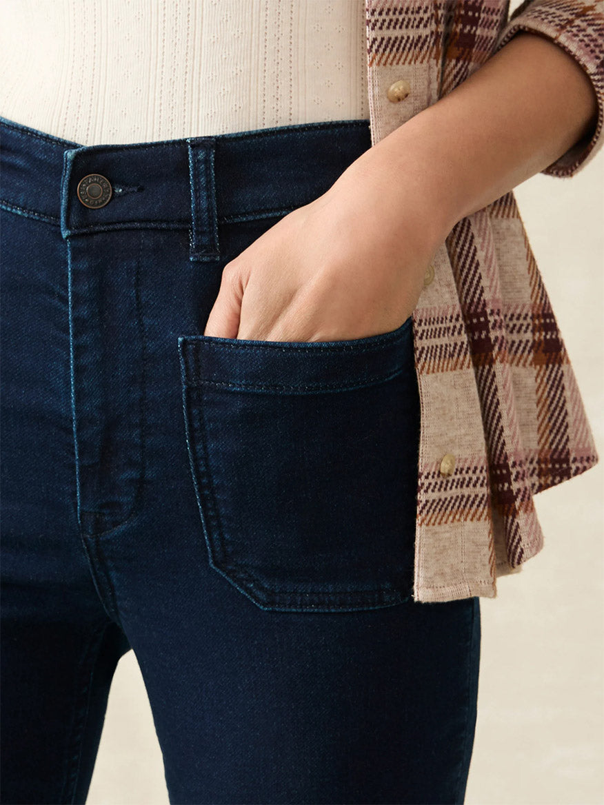 Close-up of a person wearing the Faherty Brand Stretch Terry Patch Pocket Pant in Clermont, a beige shirt, and a plaid flannel shirt, with a hand in the front pocket.