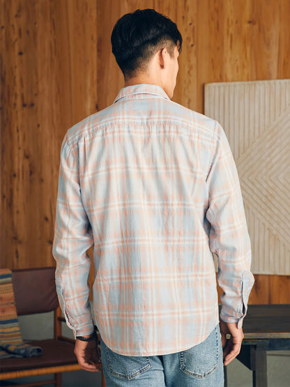 Man wearing a Faherty Brand Sunwashed Chambray Shirt in Coral Bay Plaid and jeans standing with his back to the camera in a room with wood paneling.
