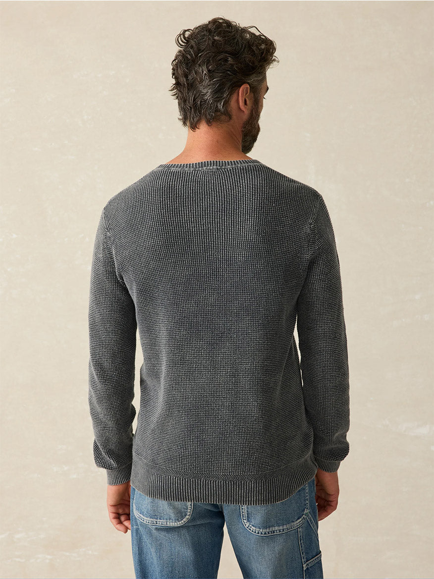 A man with short curly hair wearing a Faherty Brand Sunwashed Crewneck Sweater in Faded Black and blue jeans, photographed from the back against a neutral background, gives off a subtle vintage look.