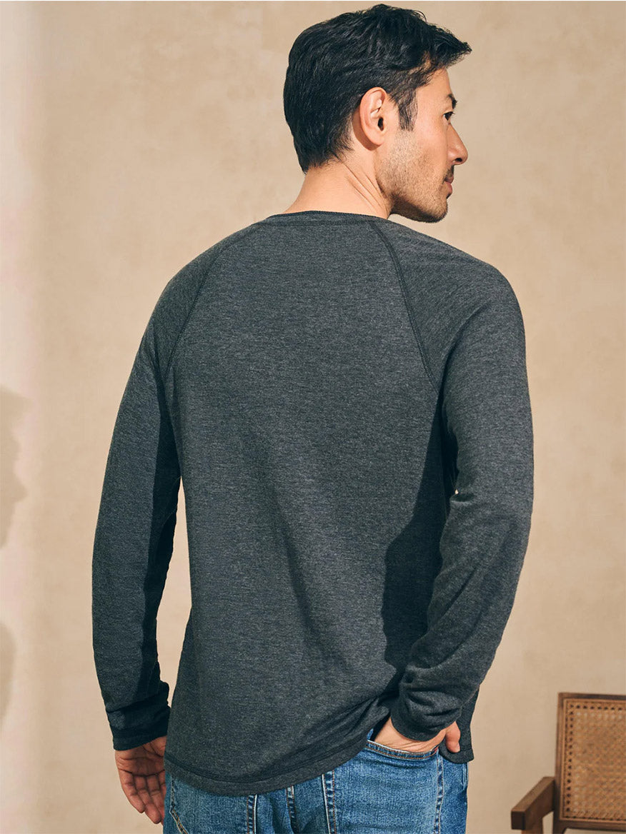 Wearing the Cloud Cotton Long-Sleeve Henley in Charcoal Heather from Faherty Brand and blue jeans, a person stands indoors facing away.