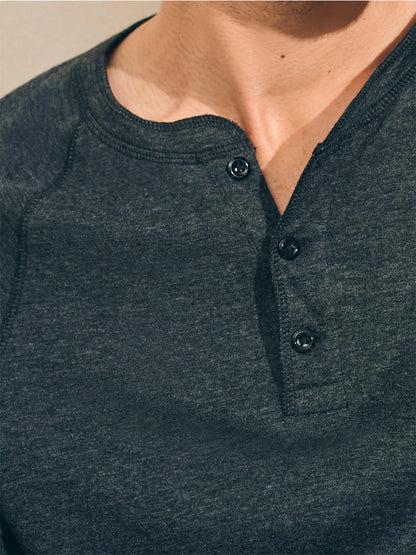 Close-up of someone wearing the Faherty Brand Cloud Cotton Long-Sleeve Henley in Charcoal Heather, featuring a buttoned collar and crafted from luxurious double-knit pima cotton.