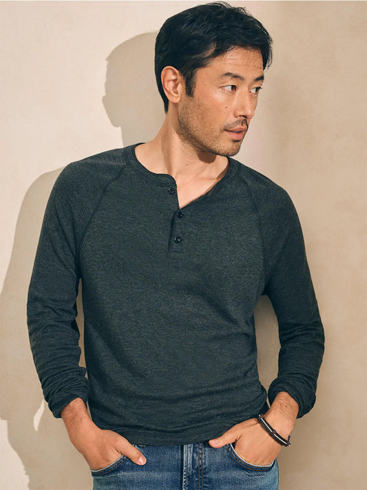 A person wearing a charcoal heather Faherty Brand Cloud Cotton Long-Sleeve Henley and jeans stands against a light background, looking to the side.