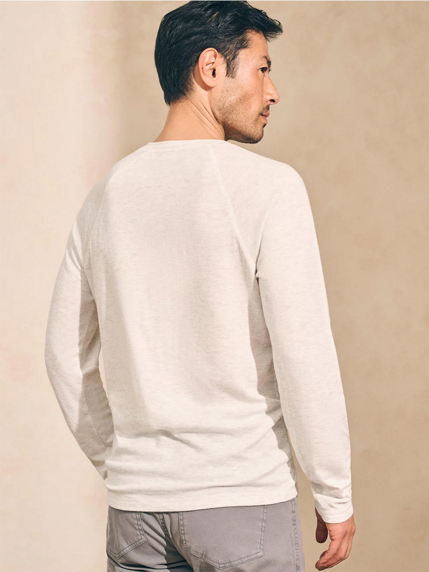 A man is standing sideways against a neutral background, wearing the Faherty Brand Cloud Cotton Long-Sleeve Henley in Ivory Heather and gray pants.