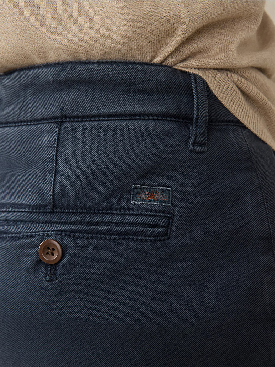 Close-up of a person in Faherty Brand Coastline Stretch Chino in Blue Nights, designed for ultimate comfort with stretch fabric and a brown button on the back pocket, effortlessly paired with a beige top.