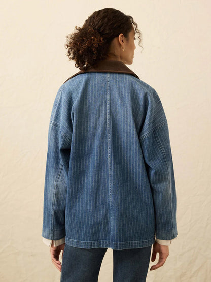Person with curly hair shown from behind, wearing the Faherty Brand Sunwashed Denim Barn Jacket in Dusk Stripe Wash with a corduroy collar and matching denim pants, set against a neutral background.