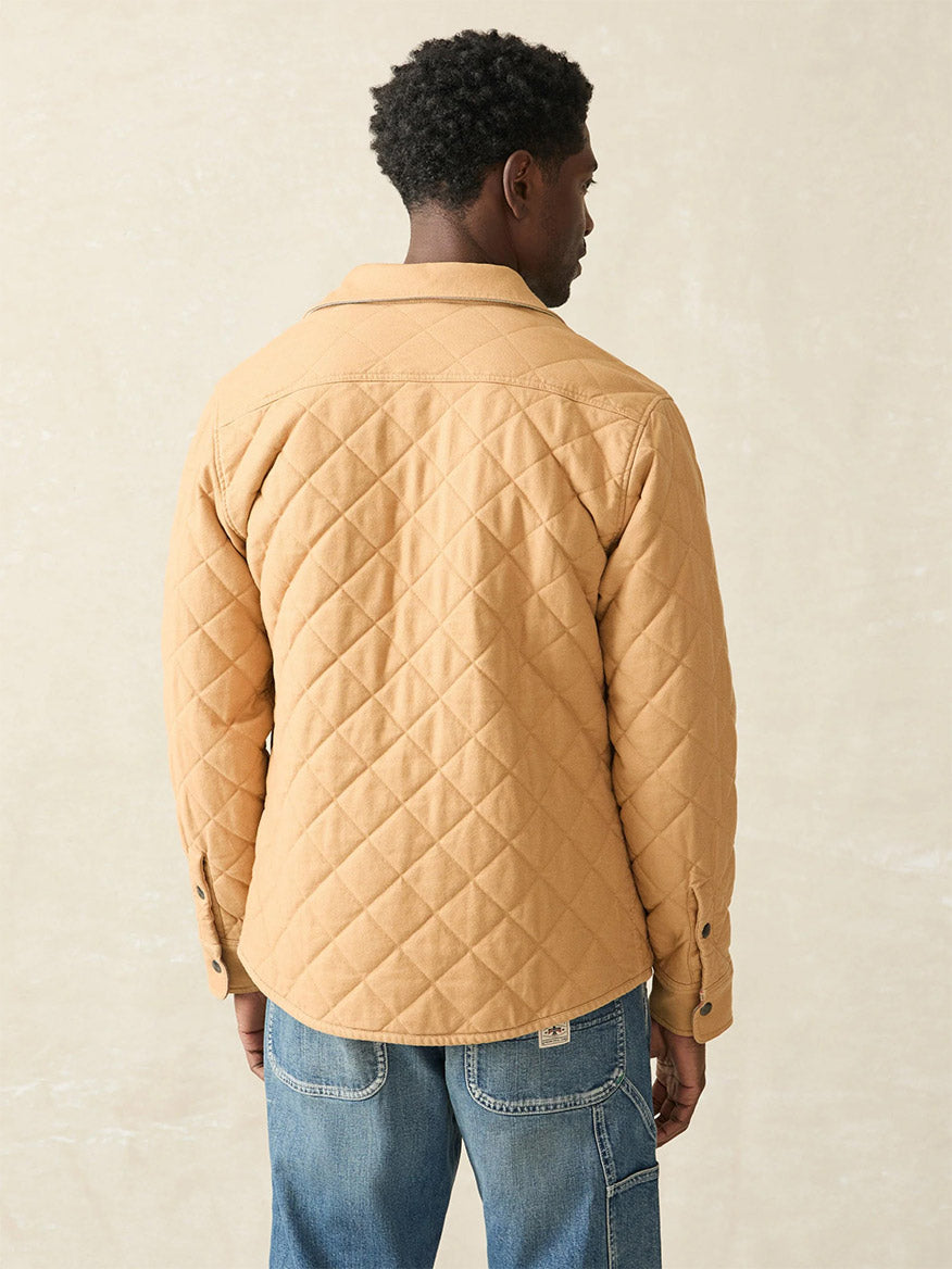 In front of a neutral background, a man faces away from the camera wearing the Faherty Brand Doug Good Feather Reversible Bondi Jacket in Dried Palm Eldorado Springs, paired with blue jeans.