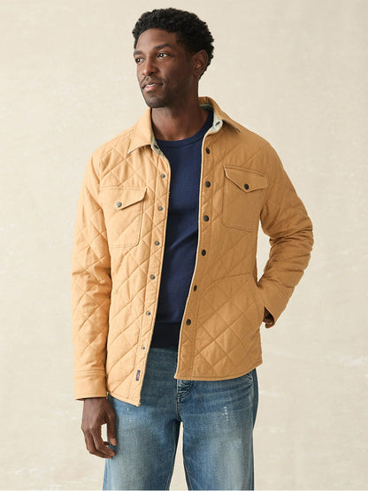 A man wearing the Faherty Brand Doug Good Feather Reversible Bondi Jacket in Dried Palm Eldorado Springs, designed by Native artist Doug Good Feather, stands confidently over a navy shirt and jeans against a plain background.