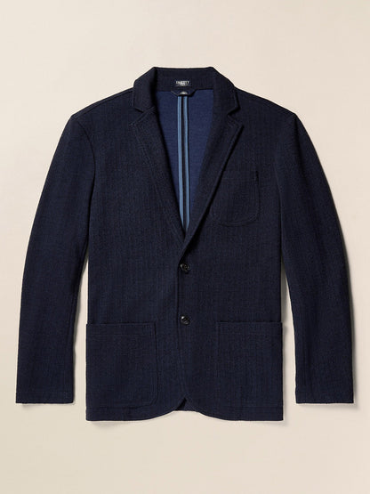 Displayed against a plain background is the Faherty Brand Inlet Herringbone Blazer in Navy Twilight, featuring two buttons, a chest pocket, and two front pockets. This versatile piece embodies Faherty's signature comfort and is perfect for any occasion.