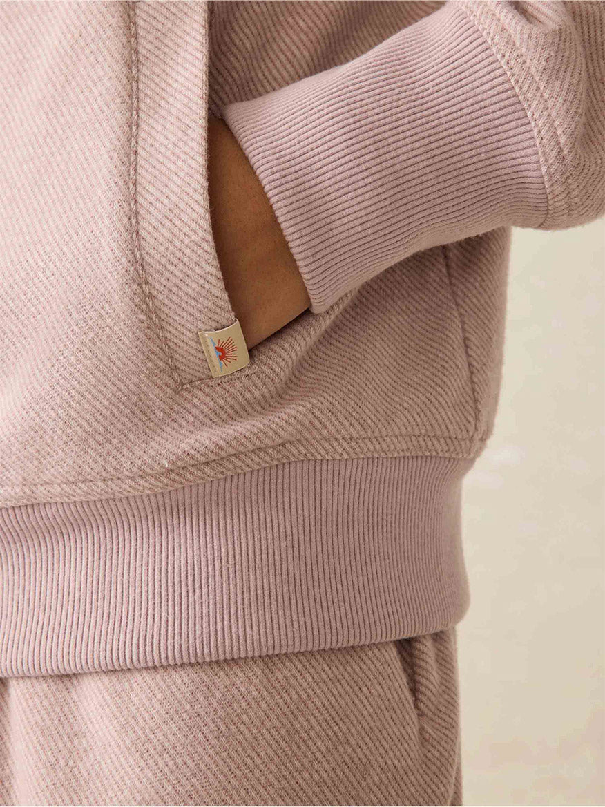 Close-up of a person wearing the Faherty Brand Legend Lounge Full Zip in Blush Twill hoodie and matching lounge set pants, with one hand in the pocket. A small tag is visible on the hoodie, highlighting its signature Legend softness and relaxed fit.