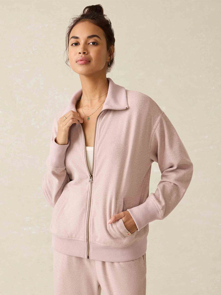 A woman wearing the Faherty Brand Legend Lounge Full Zip in Blush Twill, paired with matching pants, stands against a plain background, highlighting the signature Legend softness and its relaxed fit.