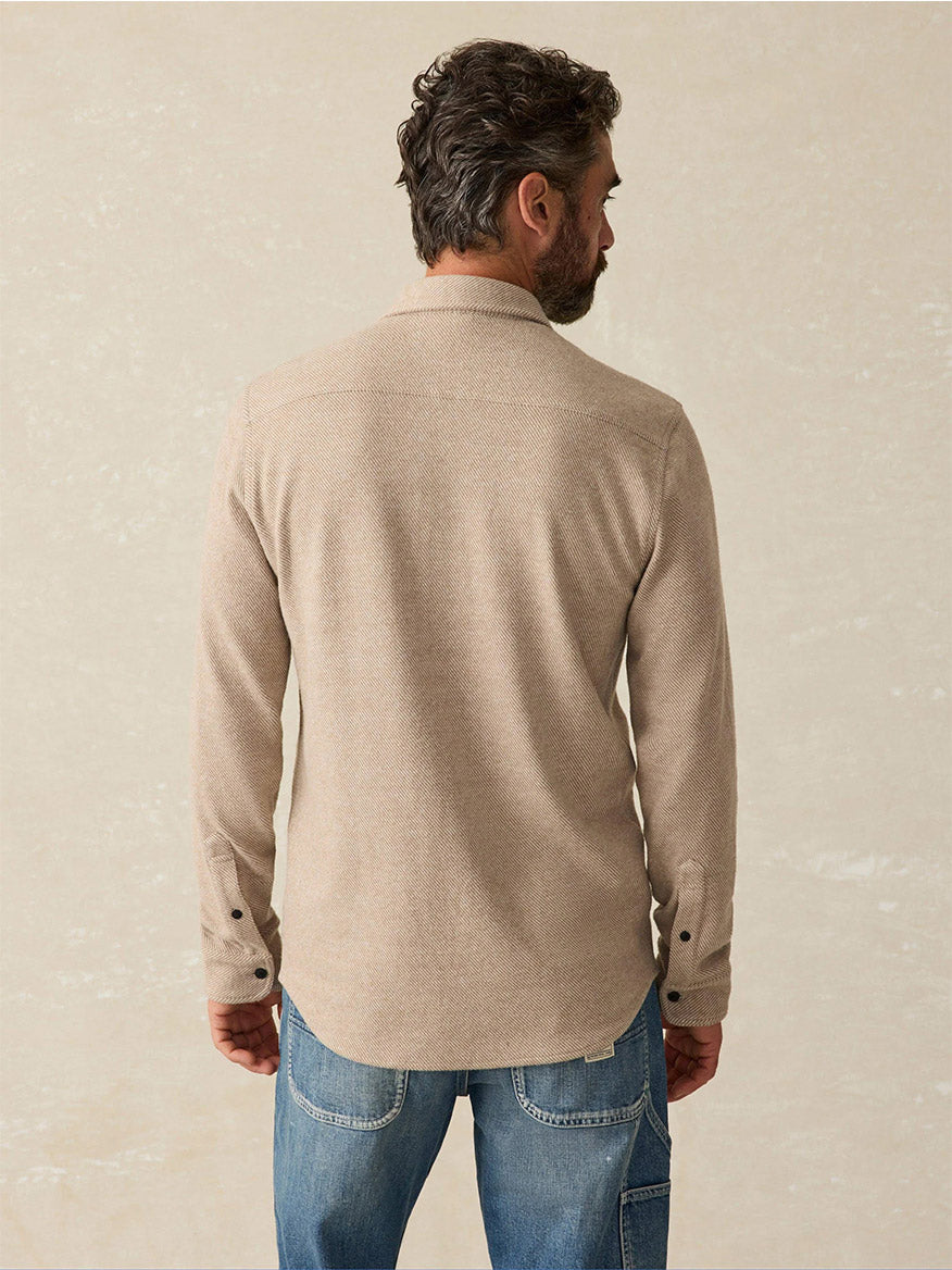 A man with dark hair, seen from behind, is wearing the Faherty Brand Legend Sweater Shirt in Timber Twill paired with blue jeans, standing against a plain light background. His outfit embodies the effortless style of Faherty with a touch of versatility, perfect for any occasion.