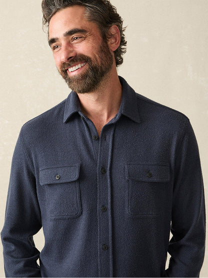 A bearded man smiles in the bestselling Faherty Brand Legend Sweater Shirt in Brighton Navy Twill, featuring chest pockets and a cozy texture, against a neutral background.