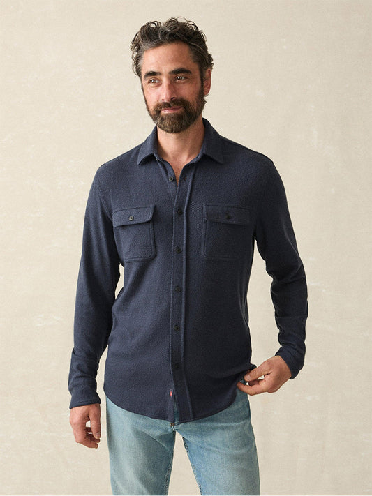 A person with a beard is wearing the Faherty Brand Legend Sweater Shirt in Brighton Navy Twill, paired with jeans, showcasing its bestselling cozy texture as they stand against a neutral background.