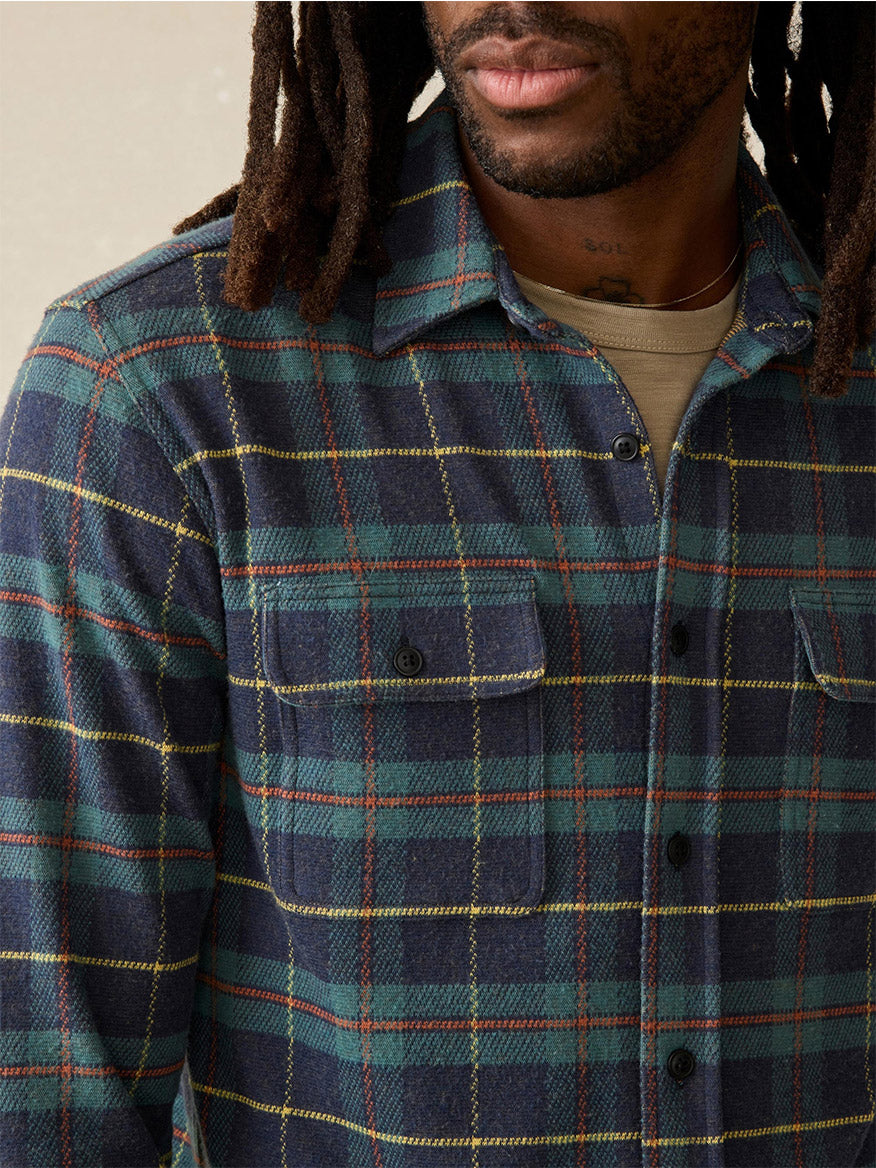 The individual is wearing the Faherty Brand Legend Sweater Shirt in Mossy Elm Plaid over a beige t-shirt, with visible dreadlocks.