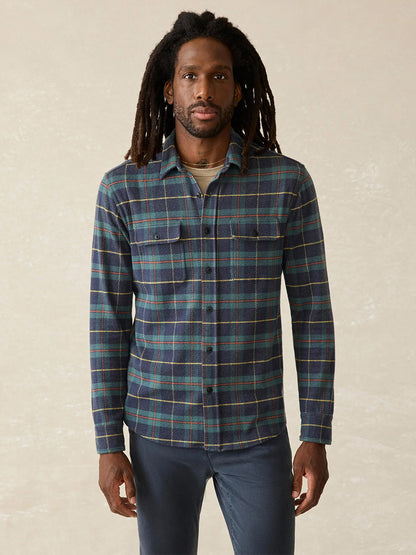 A person with long hair wearing the Faherty Brand Legend Sweater Shirt in Mossy Elm Plaid stands against a plain background.