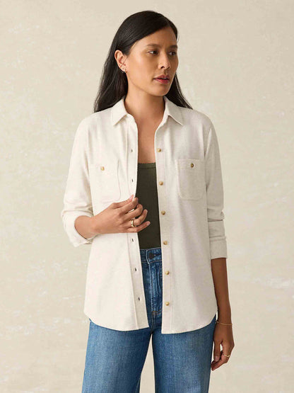 A person in a Faherty Brand Legend Sweater Shirt in Off White and jeans stands poised against a neutral background, with the custom fabric blend adding a touch of elegance to their casual look.