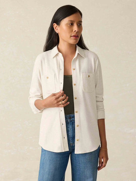 A person in a Faherty Brand Legend Sweater Shirt in Off White and jeans stands poised against a neutral background, with the custom fabric blend adding a touch of elegance to their casual look.