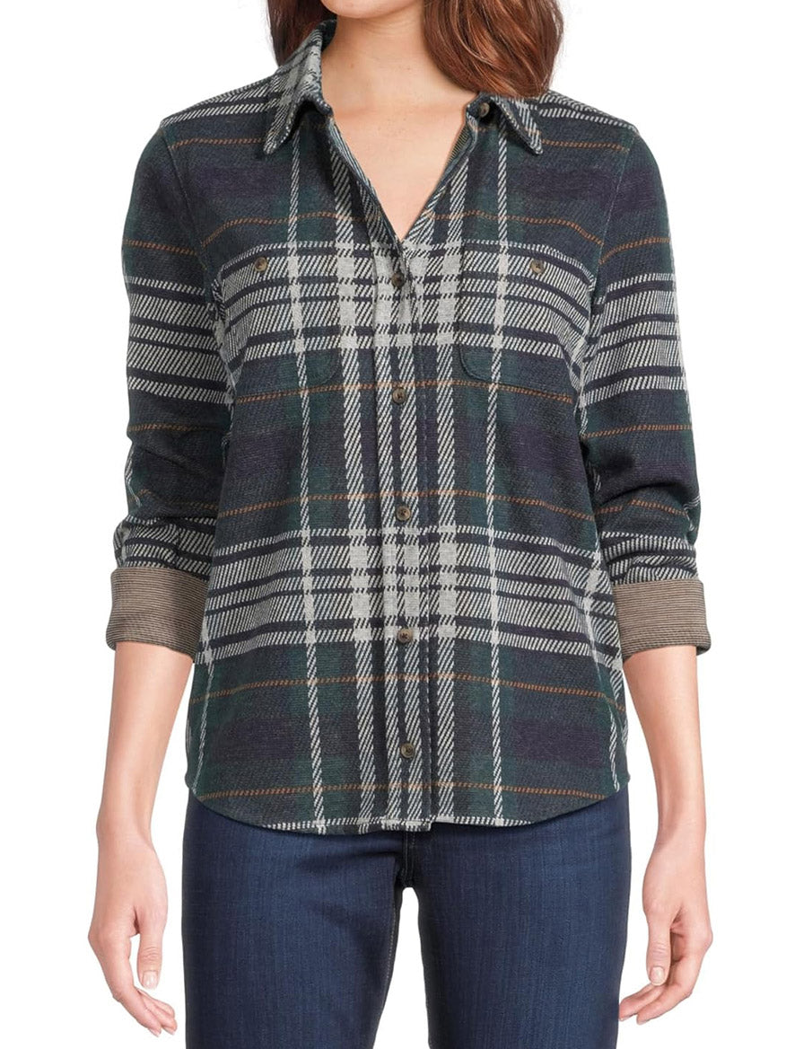 The individual is dressed in a green and blue plaid button-up shirt with dark jeans, reminiscent of the cozy allure of Faherty Brand's Legend Sweater Shirt in Blue Ridge Plaid.