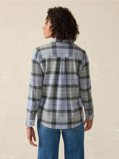 A person with curly hair, wearing the popular Faherty Brand Legend Sweater Shirt in True North Plaid and jeans, stands facing away.