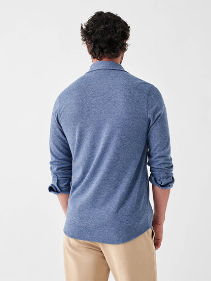 A person with short curly hair stands with their back to the camera, wearing the Faherty Brand Legend Sweater Shirt in Glacier Blue Twill, which makes a perfect layering piece, paired with light-colored pants.