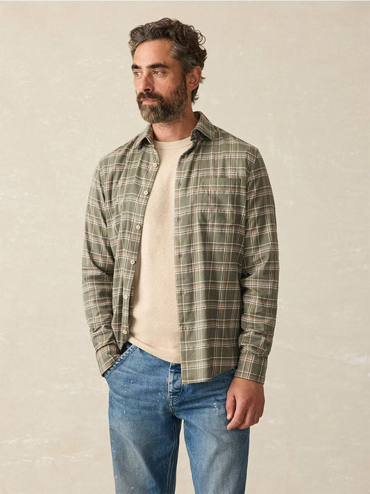 The Faherty Brand Coastline Knit Shirt in Pleasant Hill Plaid showcases its versatility as the person wears it over a beige tee and blue jeans, standing against a neutral backdrop.