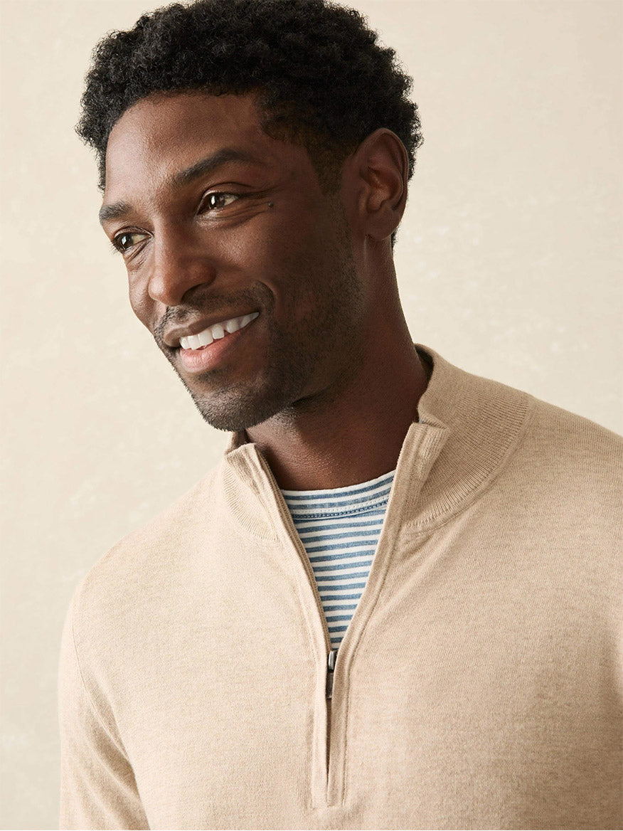 Wearing the Faherty Brand Movement Quarter Zip in Soft Dune Heather, a person smiles while looking to the side, layered over a blue and white striped shirt.