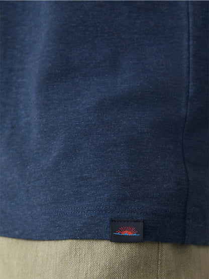 Close-up of the hem of the Faherty Brand Movement Short-Sleeve T-Shirt in Great Falls Heather, featuring a small rectangular tag with a red and blue sunrise design, worn above light-colored pants.