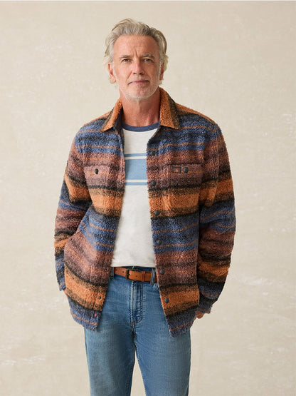 An older man in the Faherty Brand Range Fleece CPO, featuring an Autumn Horizon Stripe, over a striped shirt and jeans stands against a plain background.